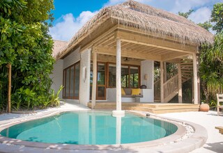 A poolside area with a thatched-roof structure, a pool, and surrounding greenery.