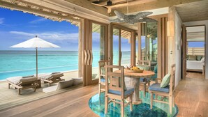 Una terraza de madera con piscina de fondo de cristal, sillas de descanso y una mesa de comedor con sillas.