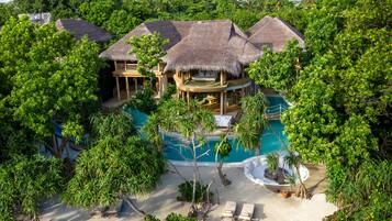 A resort with thatched-roof villas, a central pool, and lush tropical surroundings.