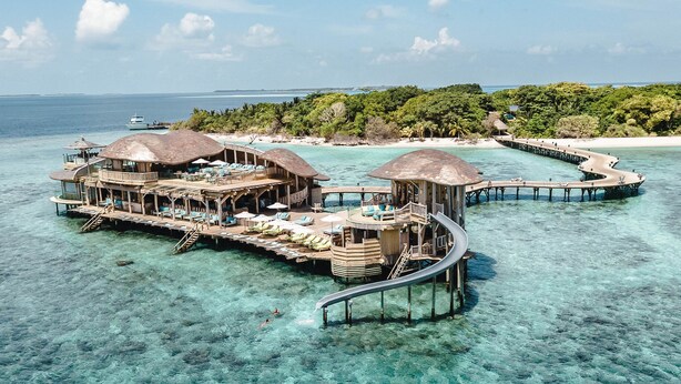 Bungalows sobre el agua con aguas azul cristalina y un muelle para barcos.