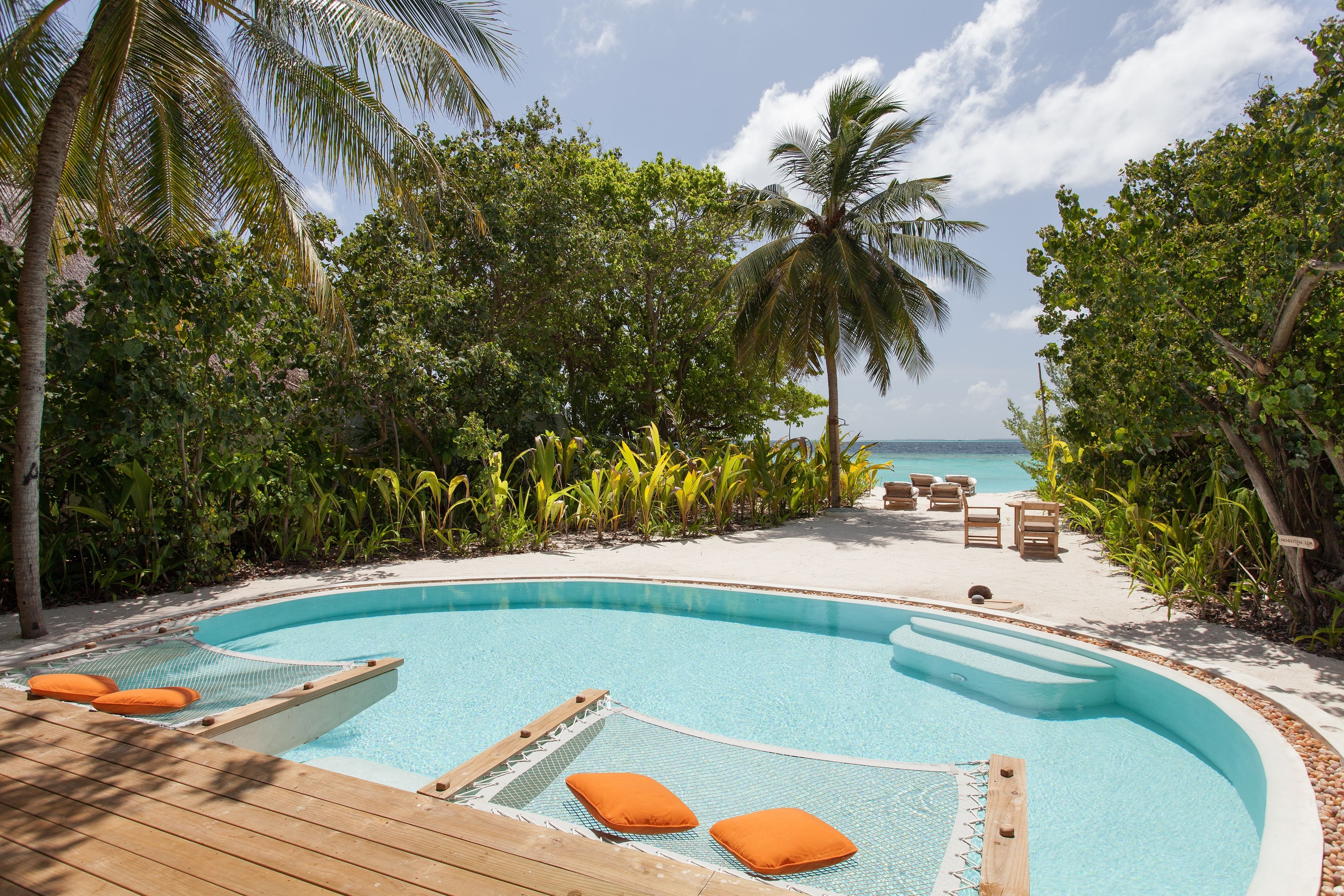 A pool surrounded by palm trees and a sandy beach.