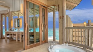 Une piscine à débordement en bois, dotée d’un jacuzzi, d’une terrasse en bois et de portes vitrées donnant sur une pièce avec vue sur l’océan.