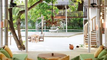 A covered outdoor area with wooden furniture, a thatched-roof structure, and a pool.