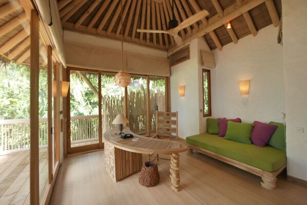 A wooden-floored room with a green sofa, a table with a lamp, and a hanging light fixture. - Soneva Fushi (Kunfunadhoo)