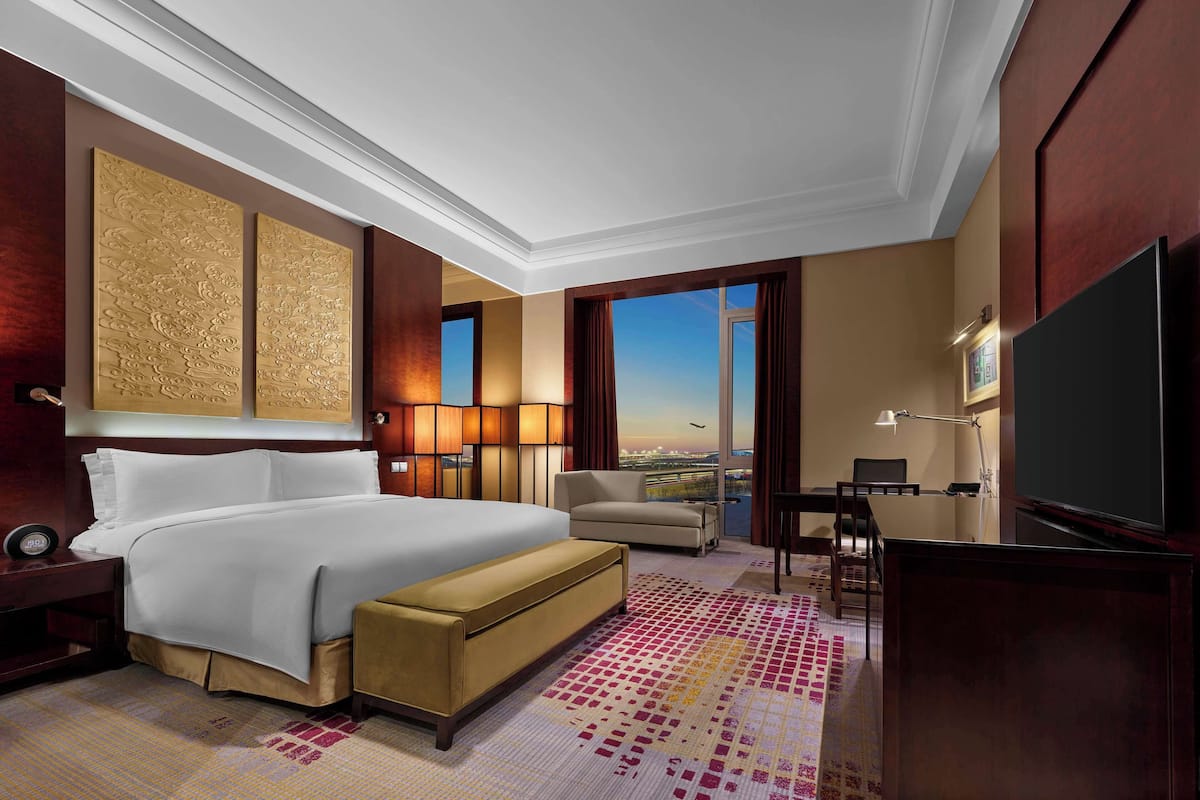 Una habitación de hotel con una cama grande, un escritorio, un televisor y vistas al aeropuerto.