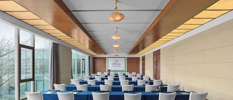 A conference room with multiple tables and chairs, large windows, and a sign for Hilton Beijing Capital International Airport.