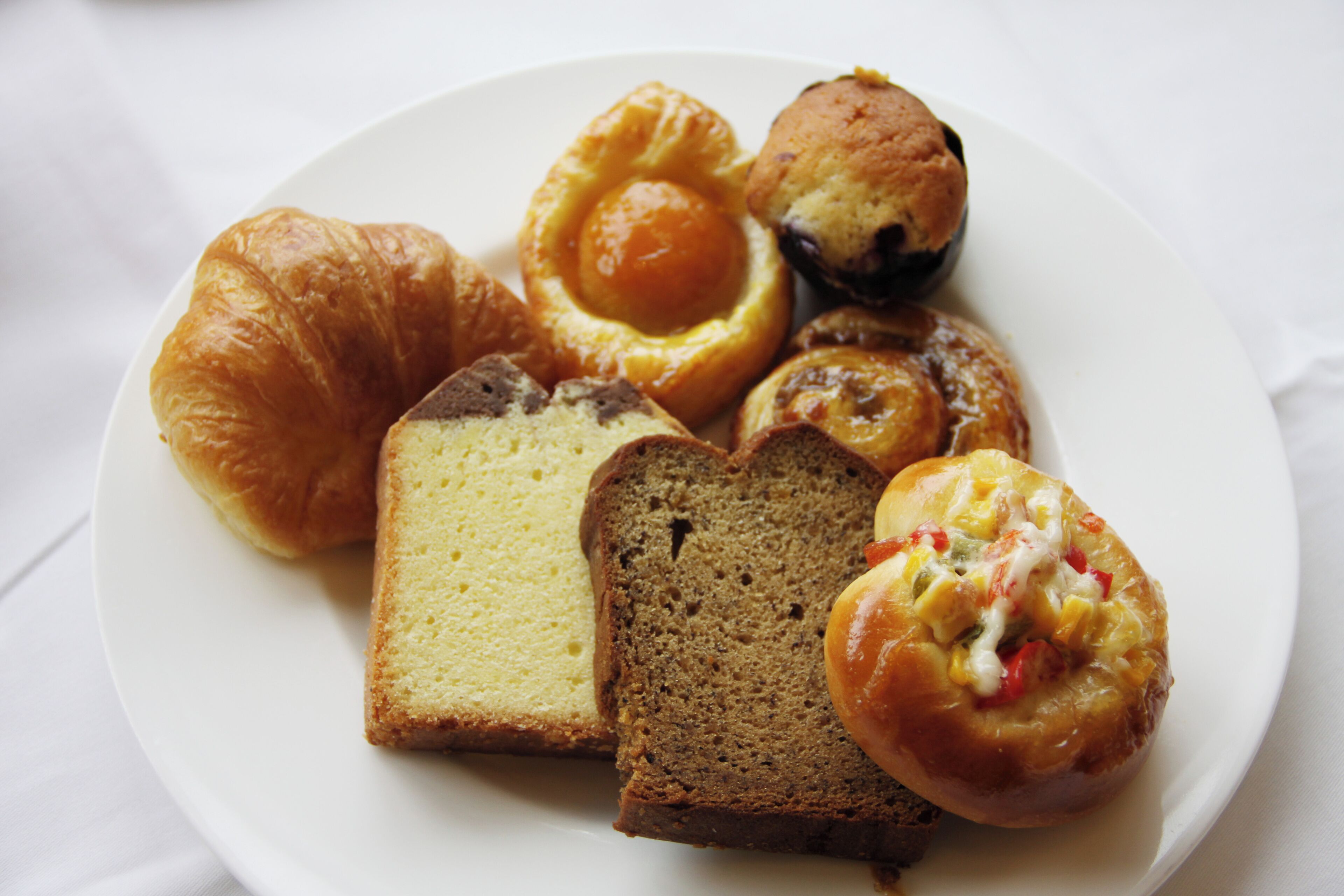 En tallerken med forskellige bagværk, blandt andet en croissant, en muffin og et rundstykke.