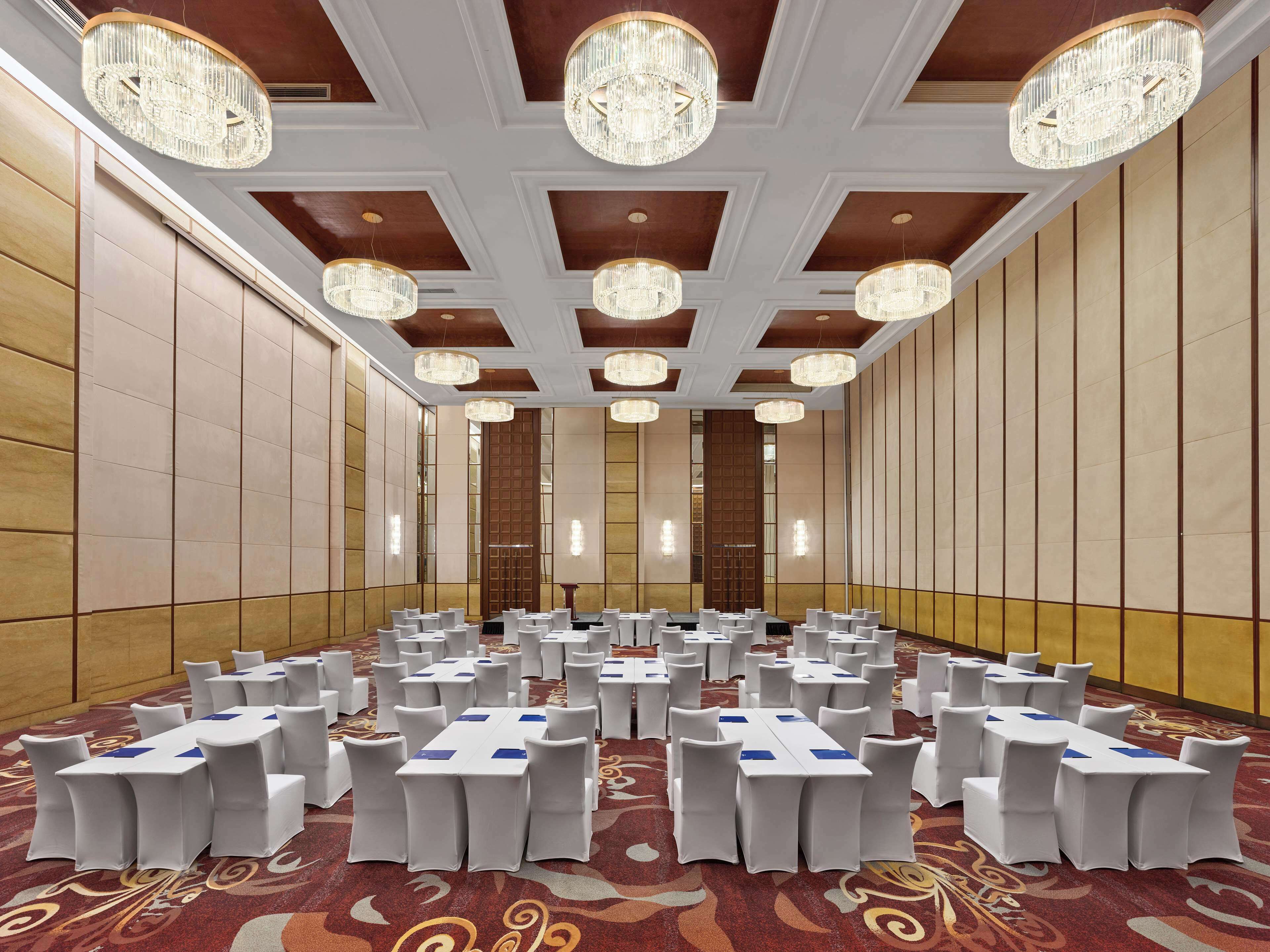 A conference room with white chairs and tables, chandeliers, and a patterned carpet.