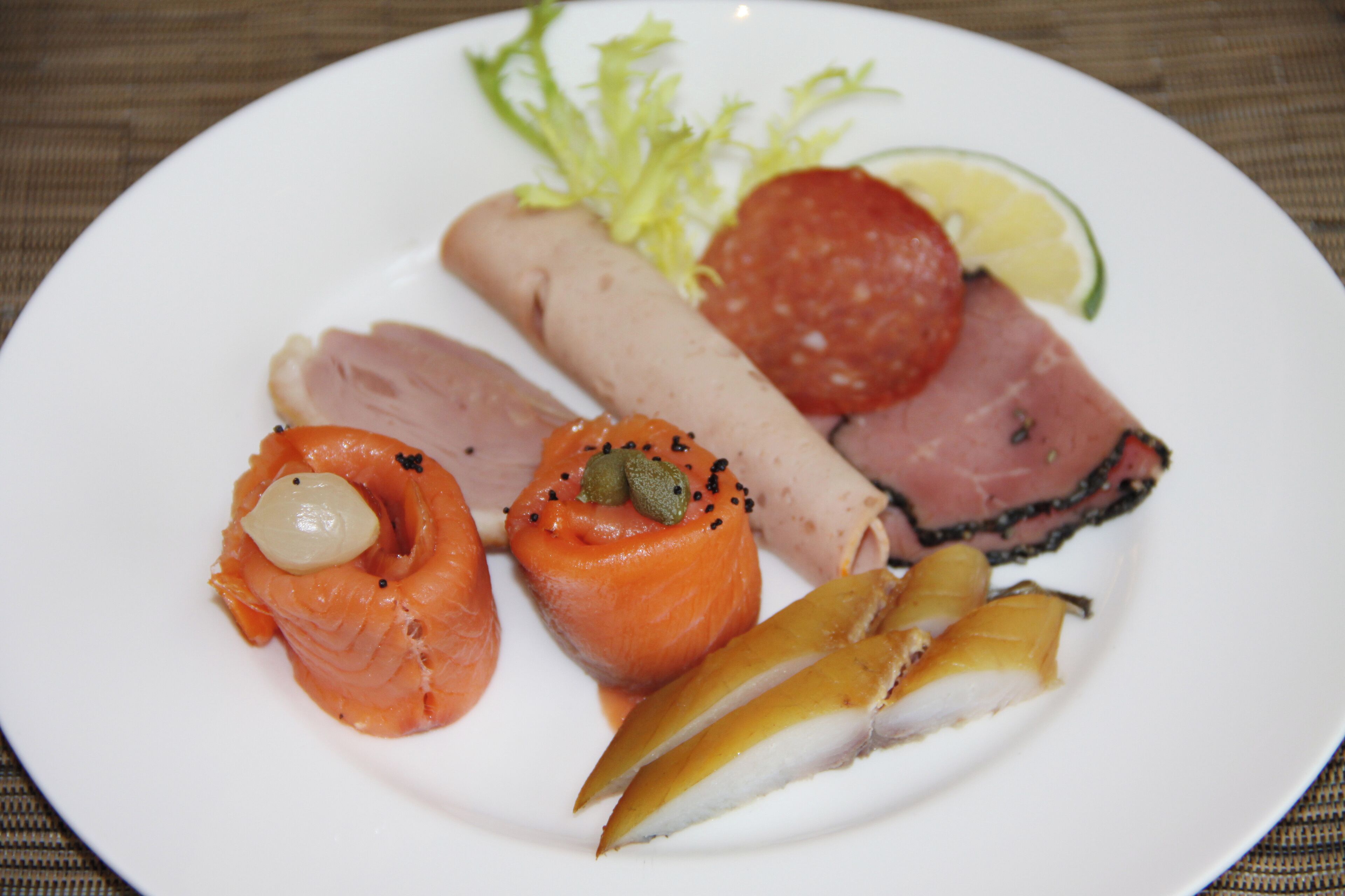Une assiette contenant différents types d’aliments, notamment du saumon, du jambon et une tranche de salami.