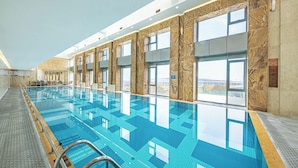 An indoor swimming pool with clear blue water, large windows, and a tiled floor.