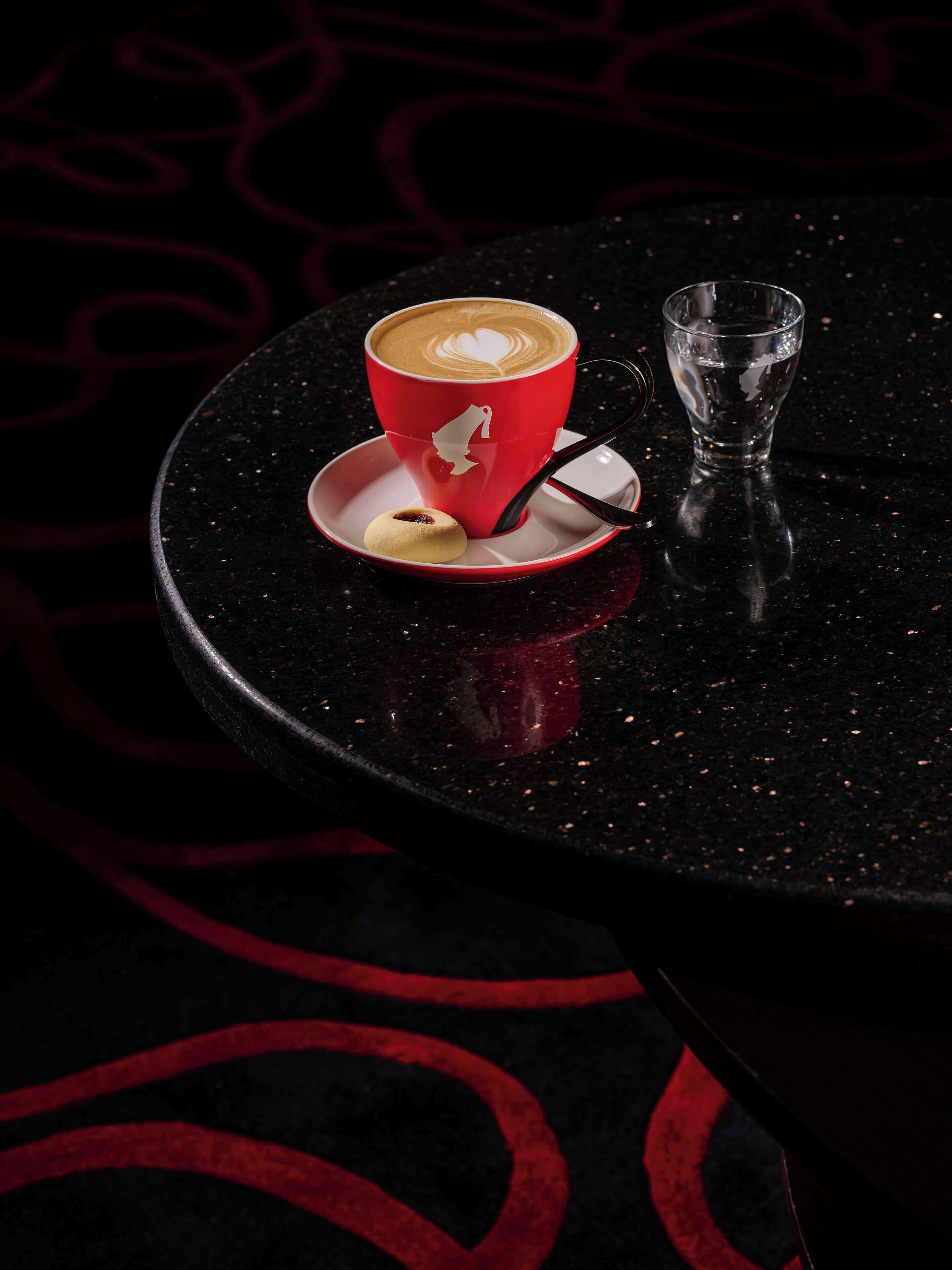 A red cup of coffee with a heart design on a black table.