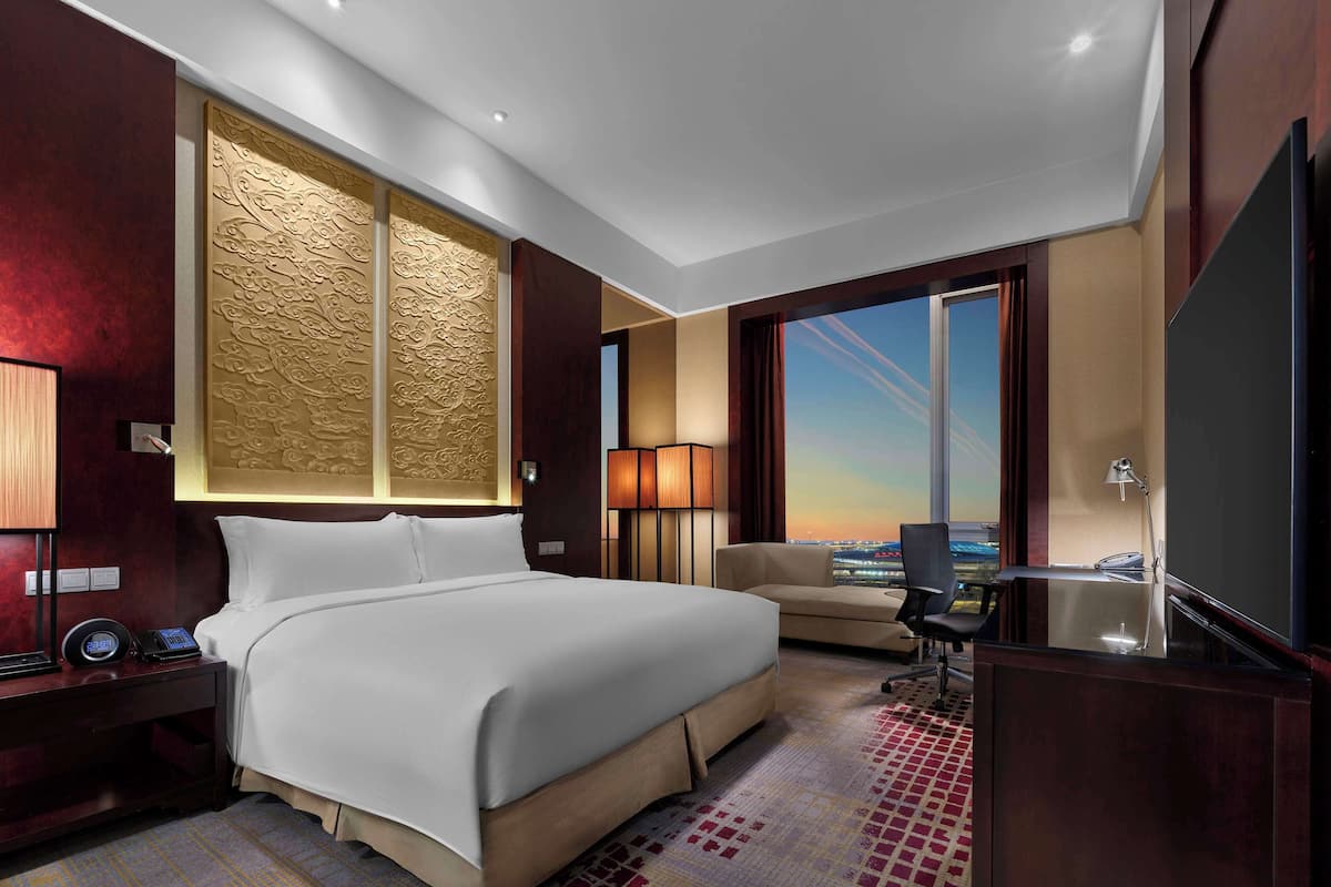 Habitación de hotel con una cama grande, un escritorio, una silla y vistas a la ciudad.