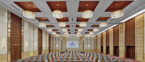 A large conference room with rows of tables, white chairs, and chandeliers.