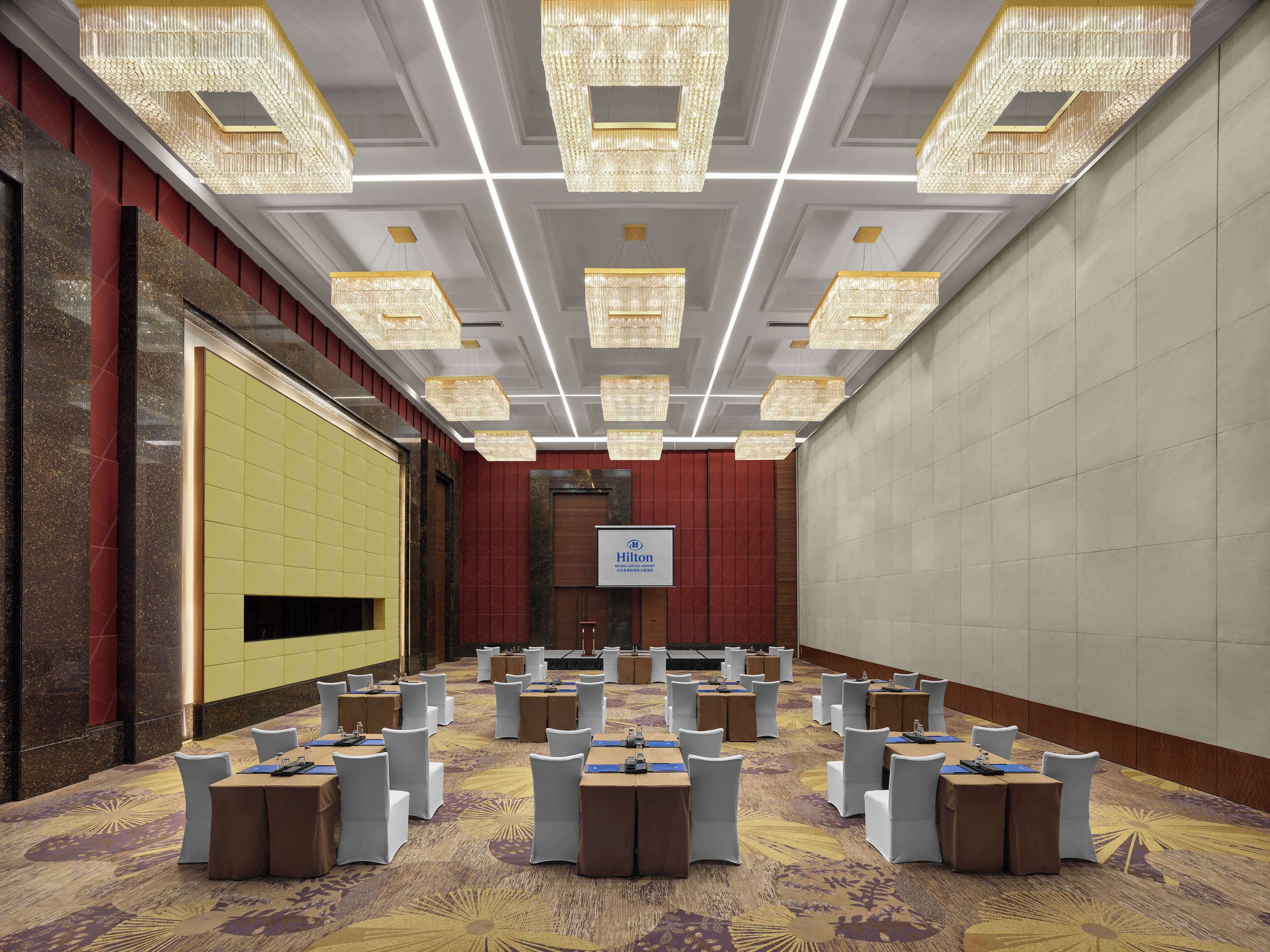 A conference room with a stage, multiple tables, and chairs, and a sign indicating Hilton services.