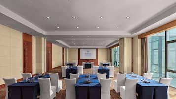 A conference room with multiple tables, white chairs, and a large screen displaying the Hilton logo.