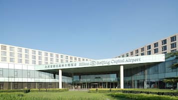 Beijing Capital Airport Hilton features a sleek glass facade and lush green surroundings.
