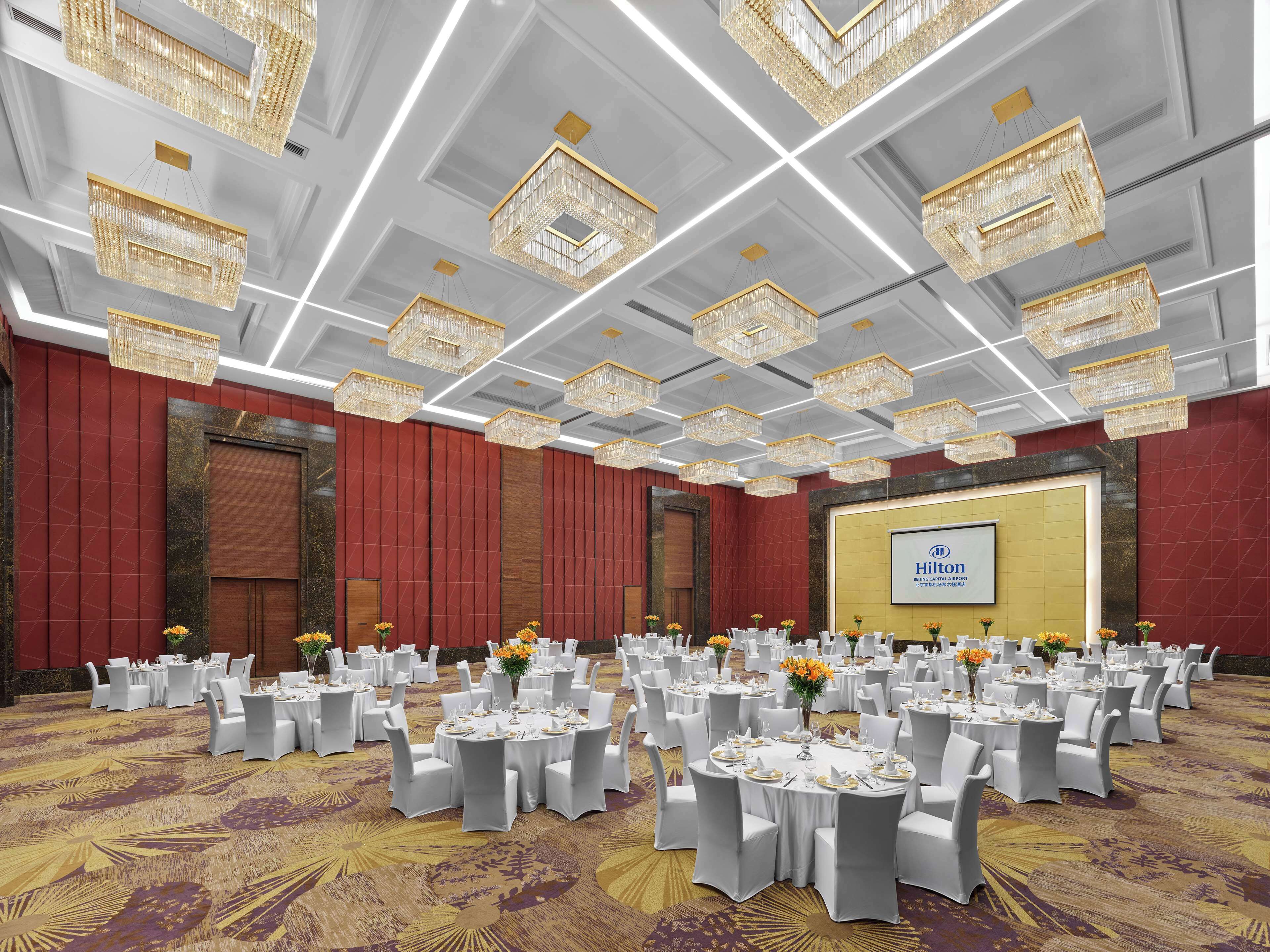A large banquet hall with round tables set for dining, chandeliers, and a Hilton sign on the wall.