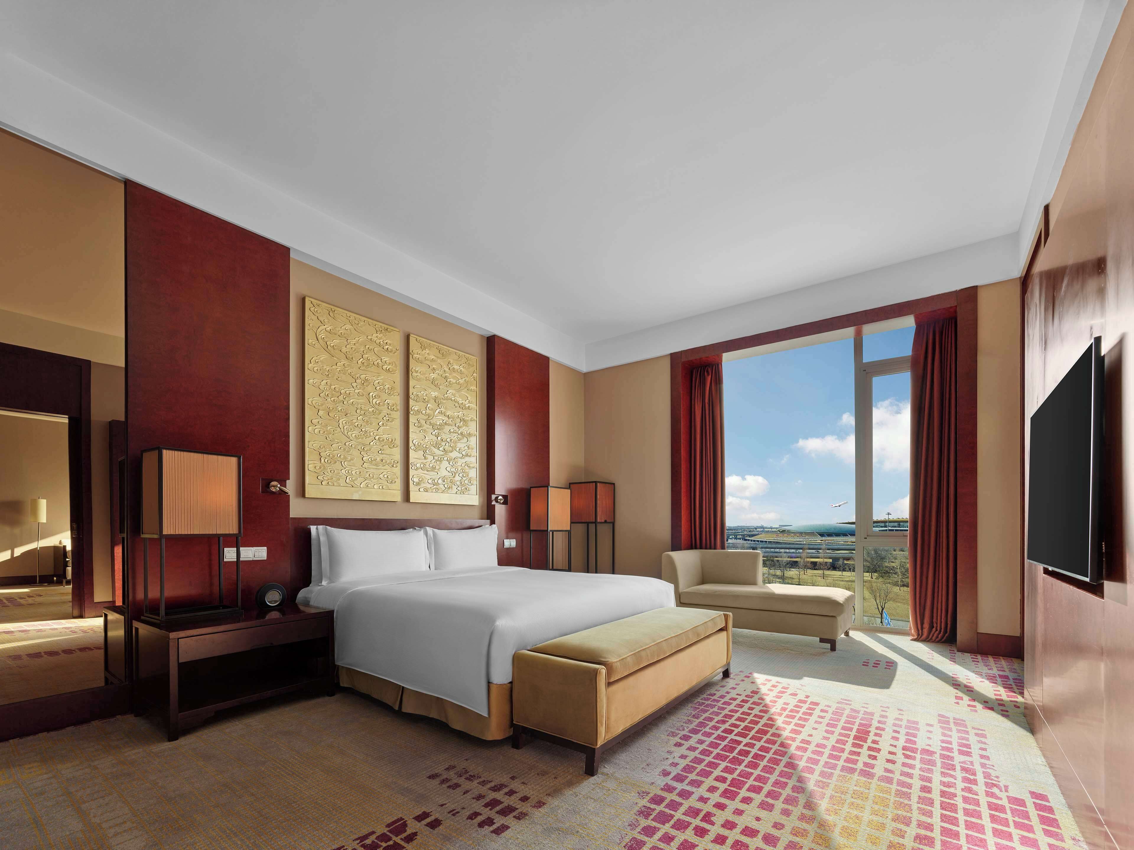 A hotel room with a large bed, a sofa, a TV, and a view of the airport.
