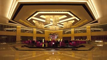 A spacious lobby with a central seating area, a chandelier, and a reflective floor.