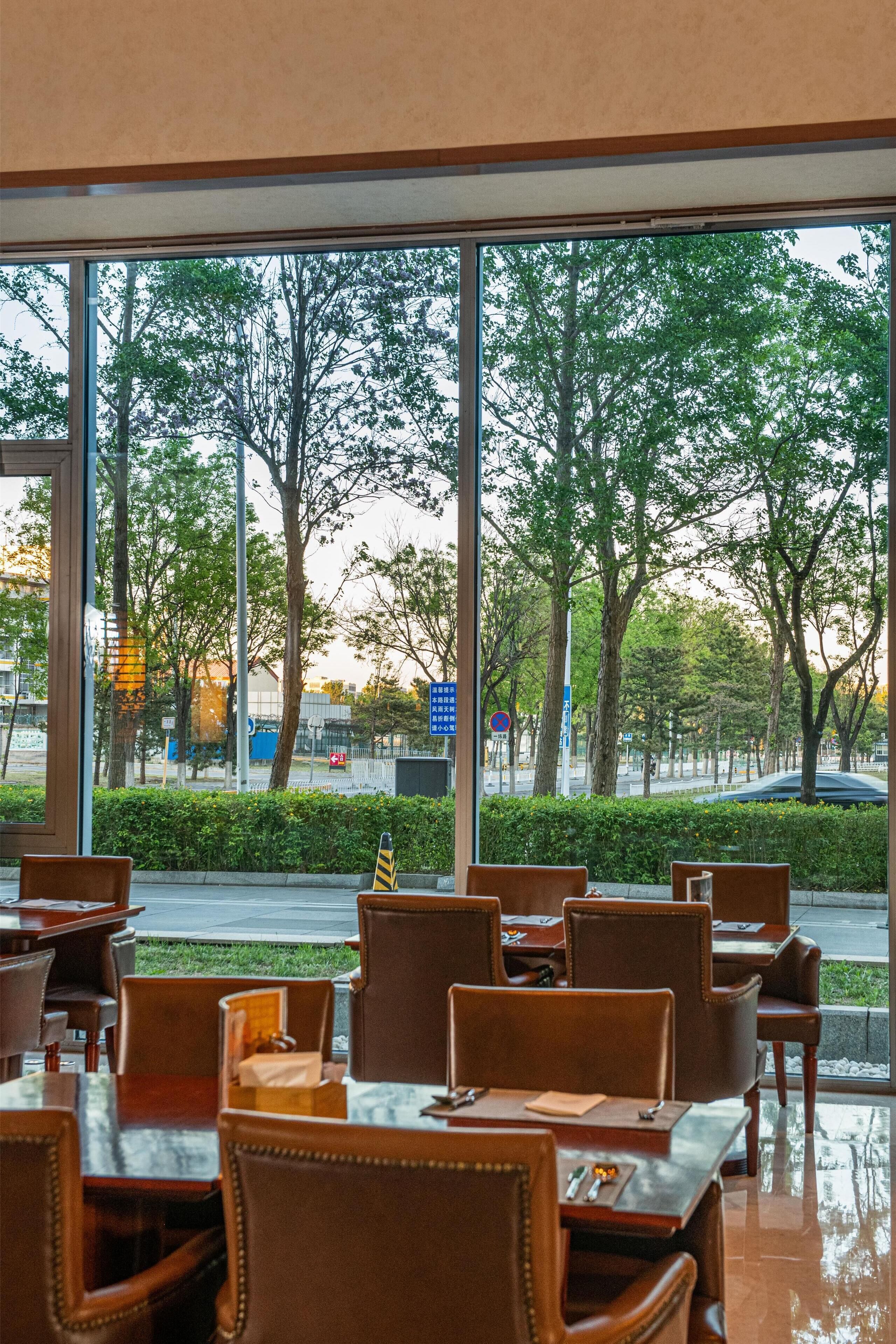 A restaurant with tables and chairs, large windows, and a view of trees and a street.