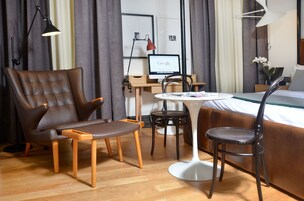 Una camera d'hotel moderna con un divano in pelle, un tavolino in legno, un tavolo da pranzo rotondo e un letto con testiera bianca.