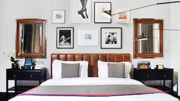 Habitación de hotel con una cama grande, dos mesitas de noche, un tocador, un espejo y cuadros en la pared.