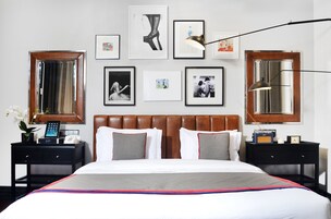Habitación de hotel con una cama grande, dos mesitas de noche, un tocador, un espejo y cuadros en la pared.