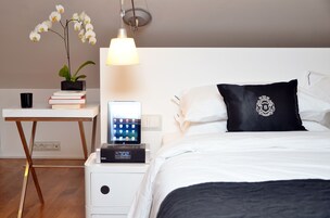 Siististi järjestetty hotellihuone, jossa on sänky, yöpöytä, lamppu ja pieni työpöytä, jonka päällä on kasvi ja kirjoja.