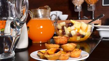 A breakfast setting with a pitcher of orange juice, a bowl of fruit, and pastries on a table.
