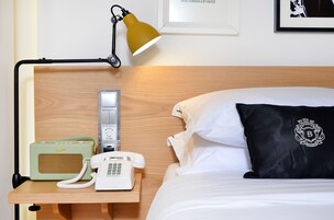 Egy szállodai szoba, melyben fából készült ágyvég található, egy éjjeli lámpa, egy régi stílusú telefon, és egy fekete párna, melyre a szálloda címerlogója van nyomtatva.
