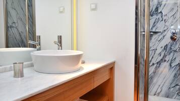 A modern bathroom with a white marble sink, wooden vanity, and a glass shower enclosure.