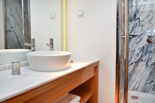 A modern bathroom with a white marble sink, wooden vanity, and a glass shower enclosure.