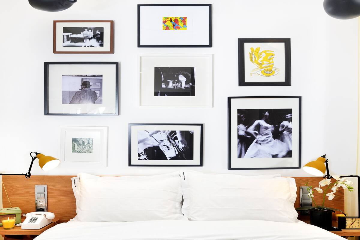 Une chambre d’hôtel comprenant un lit, une table de chevet, une lampe et un mur décoré de photographies encadrées.