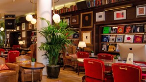 Un espace salon accueillant avec des canapés en cuir, des fauteuils rouges, une grande plante en pot et une bibliothèque remplie de livres et de photos encadrées.