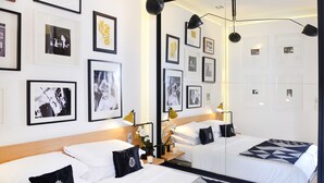 Une chambre d’hôtel avec deux lits, un grand miroir et plusieurs photographies encadrées accrochées aux murs.
