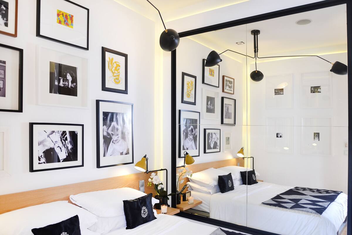 Une chambre d’hôtel avec deux lits, un grand miroir et plusieurs photographies encadrées accrochées aux murs.