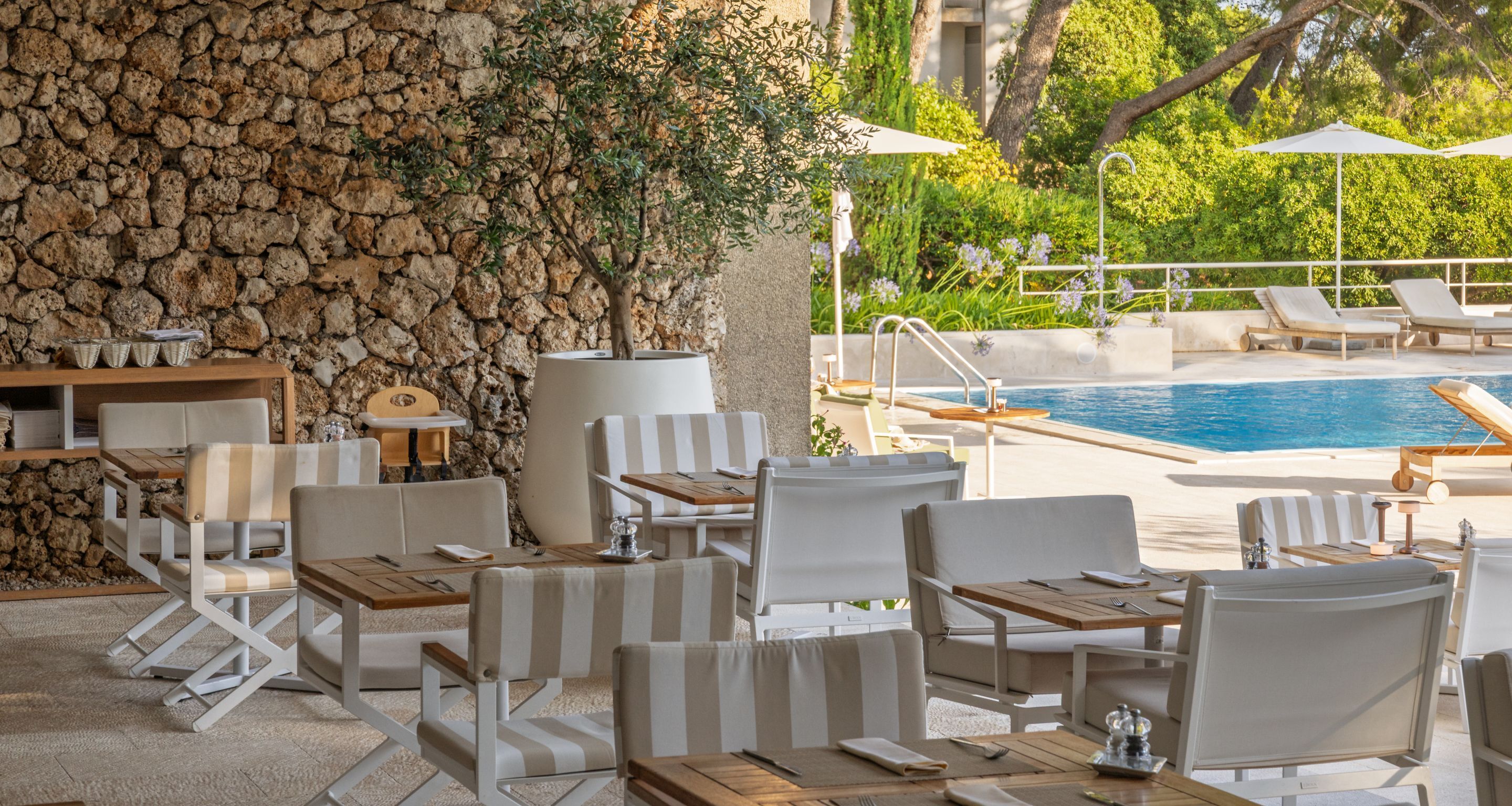 A poolside area with white striped lounge chairs, a stone wall, and a view of the pool.