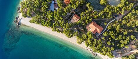 An aerial view of a coastal property with a beach, trees, and buildings.