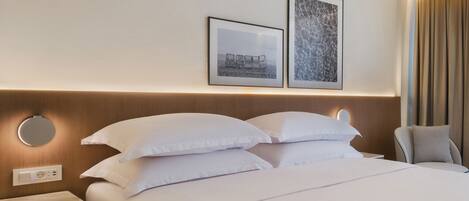A neatly made bed with white linens, a round bedside table with a lamp, and two framed pictures on the wall.