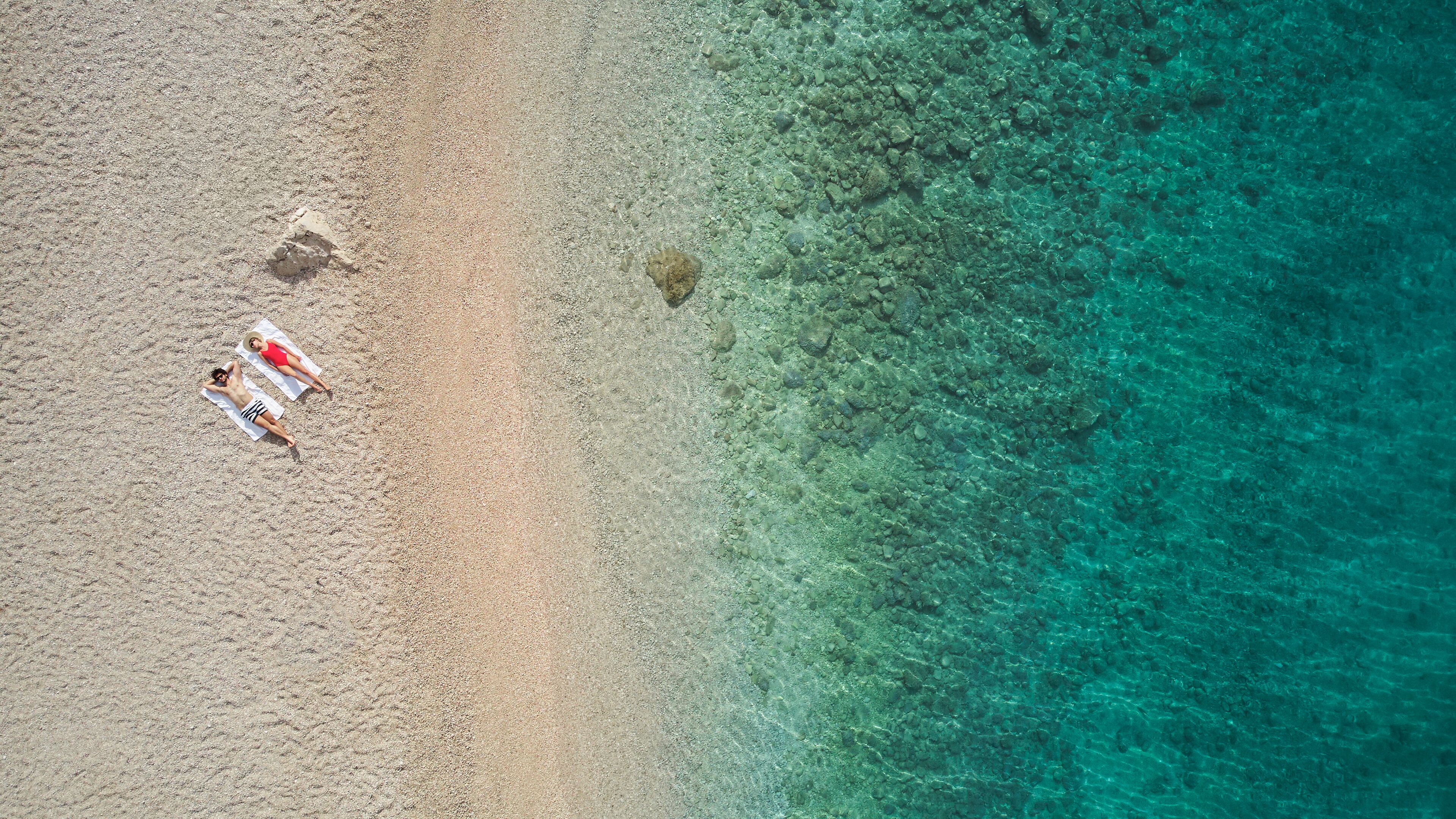 Vue aérienne d’une plage aux eaux turquoise et limpides, bordée d’un rivage sablonneux.