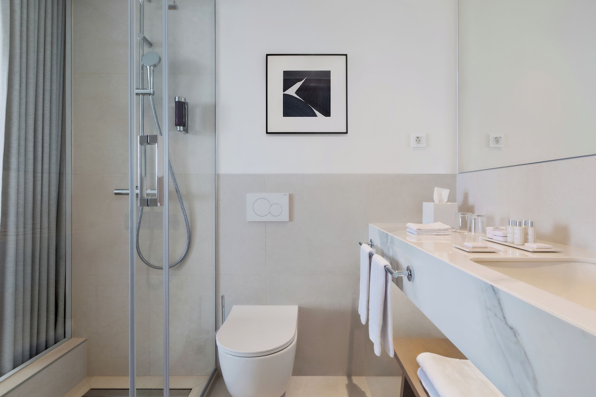 A modern bathroom with a glass-enclosed shower, a white toilet, and a marble countertop with toiletries.