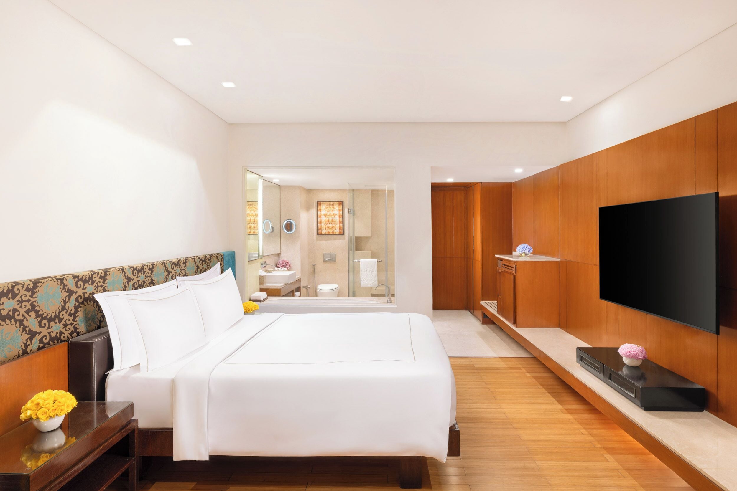 A modern hotel room with a large bed, a TV, and a bathroom visible through a glass door.