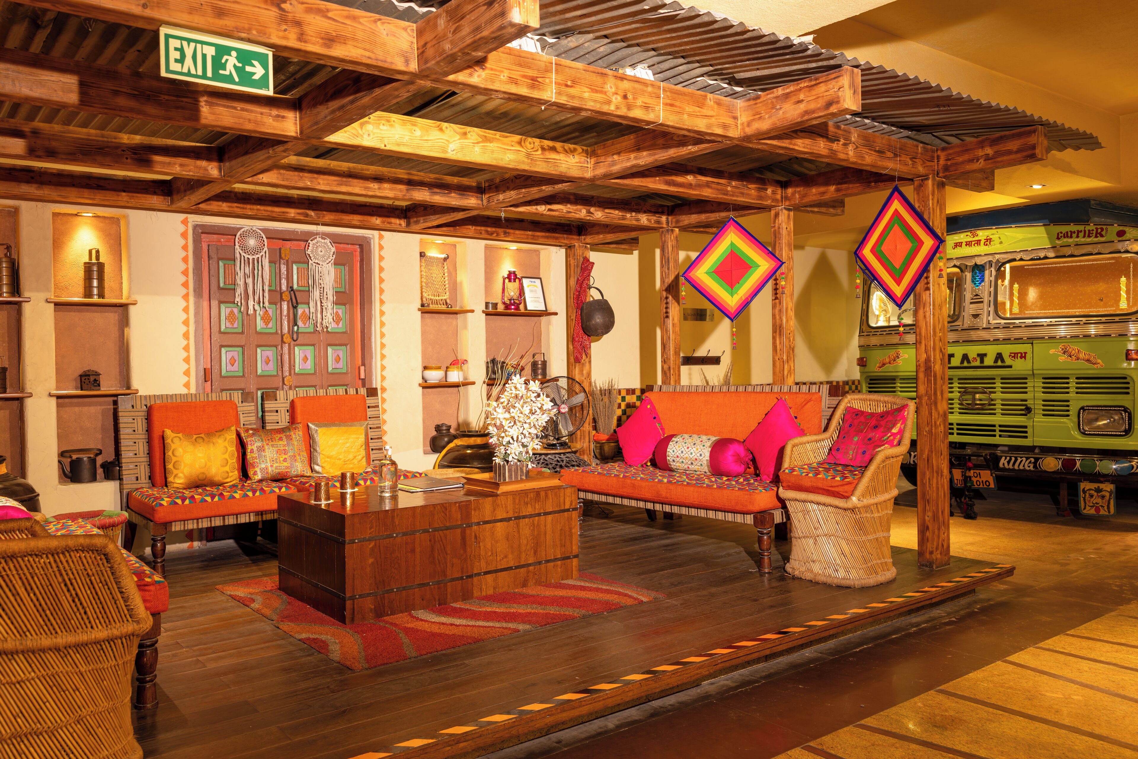 A traditional interior with wooden beams, a sofa set, a green bus, and an exit sign.
