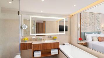 Un baño moderno con un espejo grande, un tocador de madera, una bañera y una cama con cabecera floral.