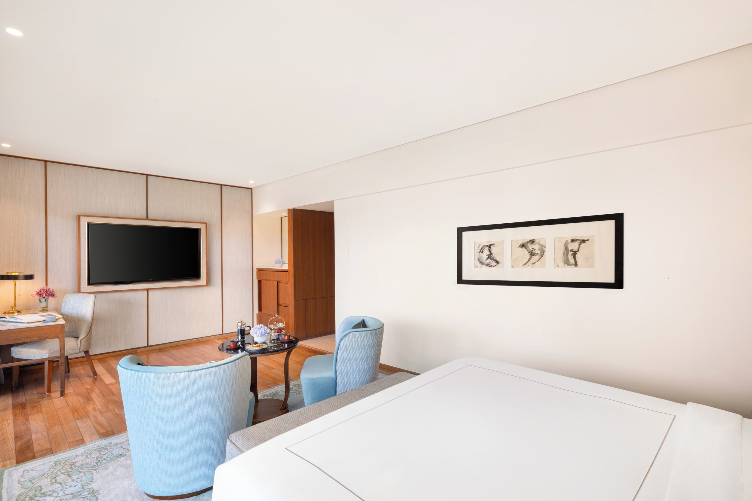 A modern hotel room with a flat-screen TV, a dining area with a table and chairs, and a framed artwork on the wall.