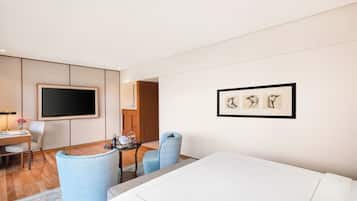 Una habitación de hotel moderna con un televisor de pantalla plana, un área de comedor con mesa y sillas, y una obra de arte enmarcada en la pared.