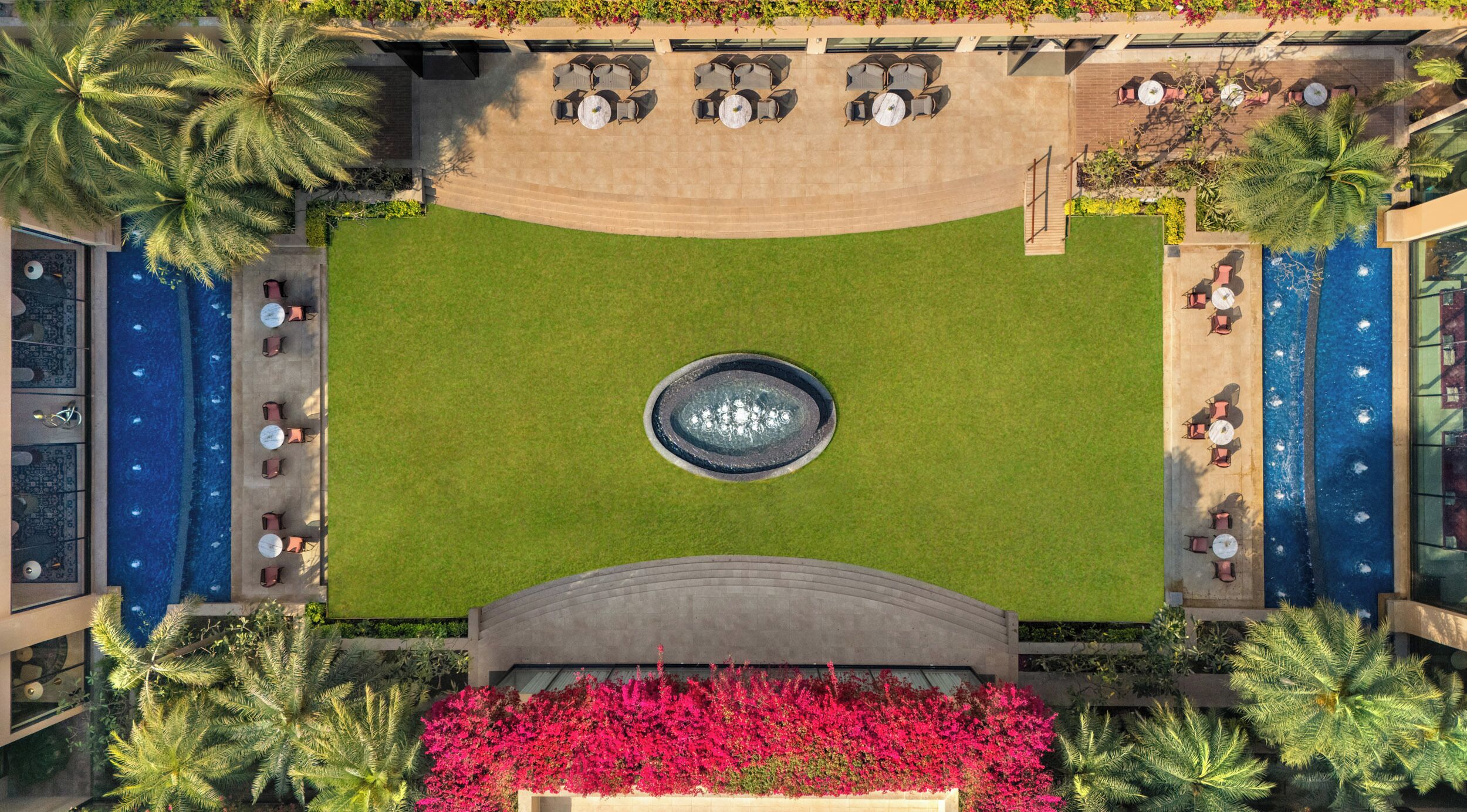 An aerial view of a resort with a central pool, surrounding lounge areas, and tropical landscaping.