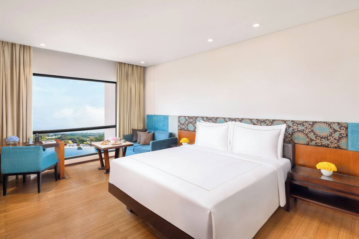 A hotel room with a large bed, a desk, a chair, and a view of the outdoors.