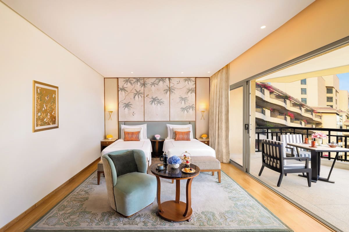 A hotel room with two beds, a small table, a chair, and a balcony with a table and chairs.