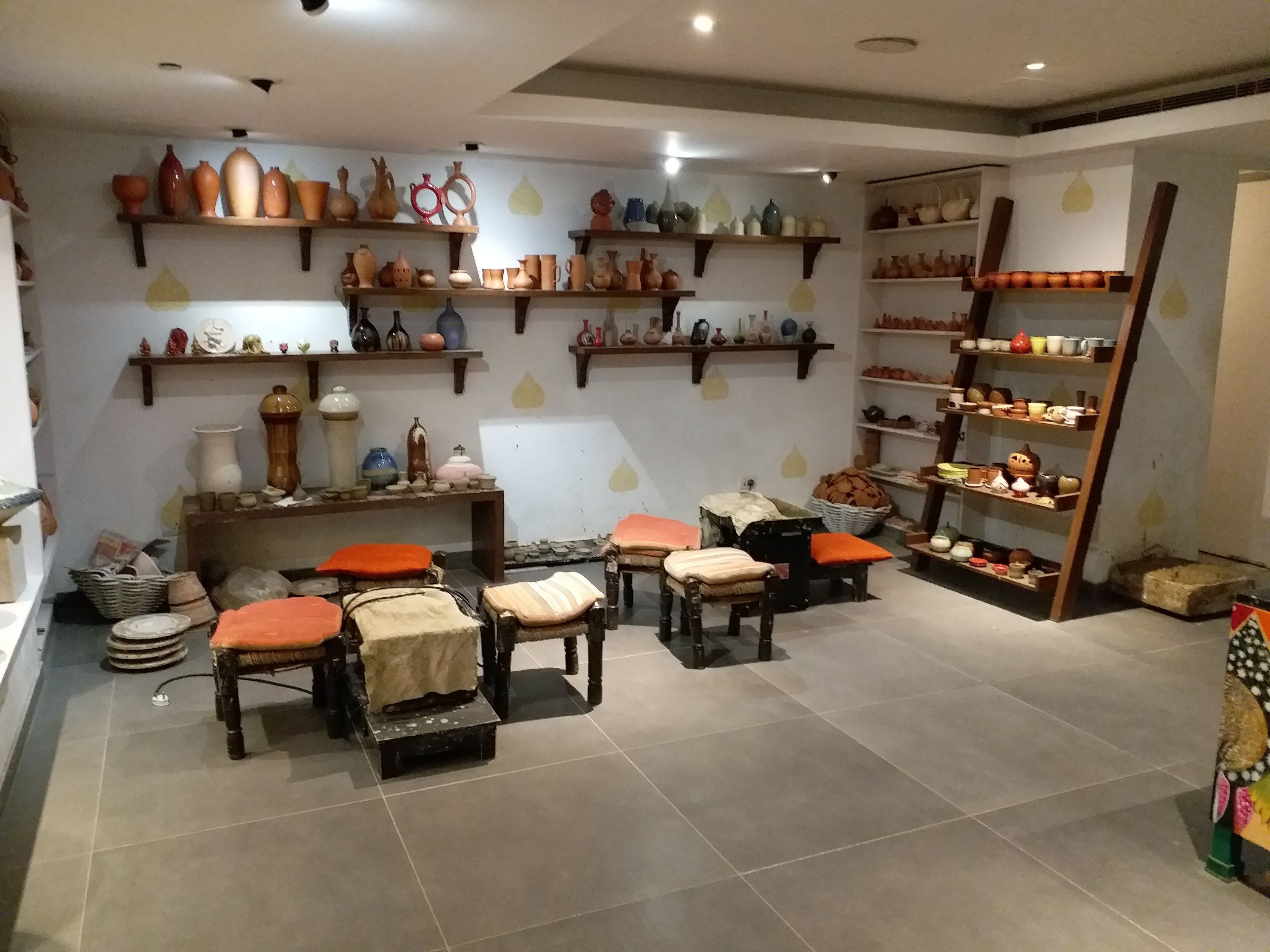 Une boutique de poterie où l’on trouve des étagères remplies de céramiques et un espace détente avec des fauteuils confortables.